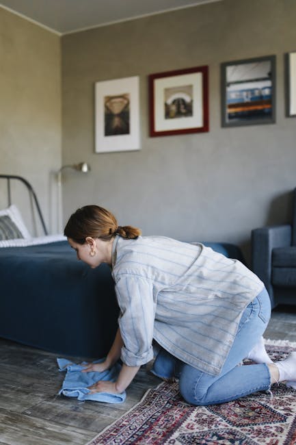 A person wearing a grey jumpsuit is engaged in deep cleaning in an empty auditorium with dark blue walls, black flooring, and tiered seating. They are using a professional vacuum cleaner to remove dust or debris from the carpeted surface, which appears clean and well-maintained under soft lighting. The room features modern design elements, with visible structural beams and step-up seating in the background. This demonstration of surface cleaning aligns with the services offered by Carpet Cleaning Hounslow, emphasizing thorough sanitisation and maintenance of large, carpeted areas in commercial spaces.